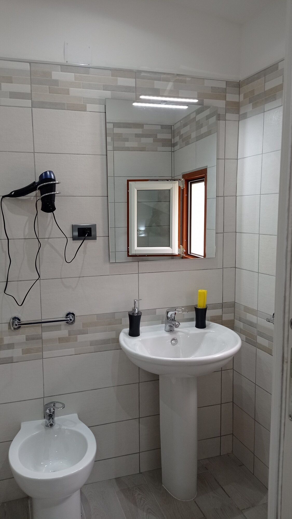 A bathroom with a pedestal sink, a wall-mounted hairdryer, a mirror, and a bidet.