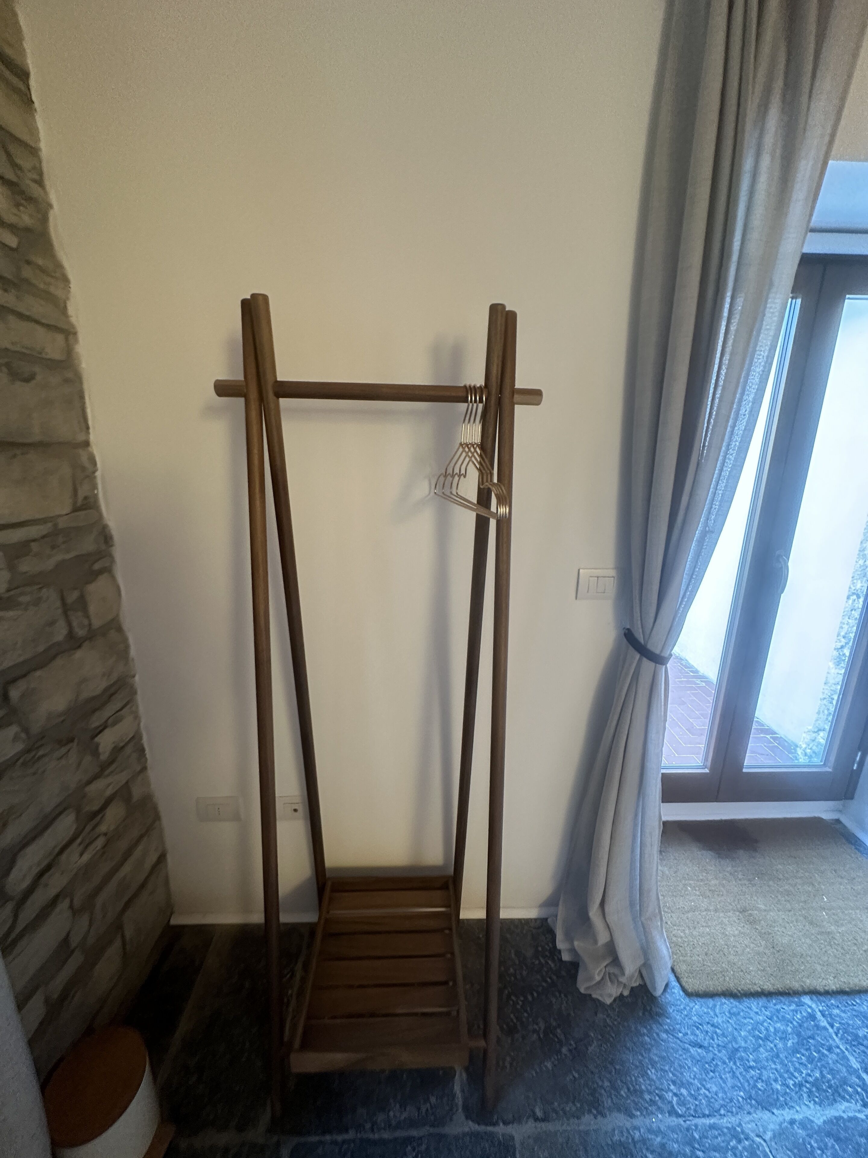 A room with a wooden swing chair, stone wall, and a window with curtains.