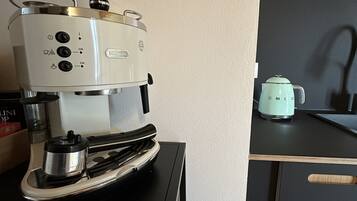 A kitchen with a coffee maker on a black countertop and a kettle on the stove.