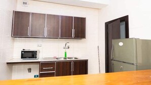 Cocina compacta con armarios de madera oscura, un lavamanos de acero inoxidable y un microondas integrado.
