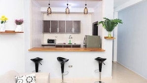Una cocina moderna con encimera de madera, un microondas y un lavabo. Hay tres taburetes negros frente a la encimera.