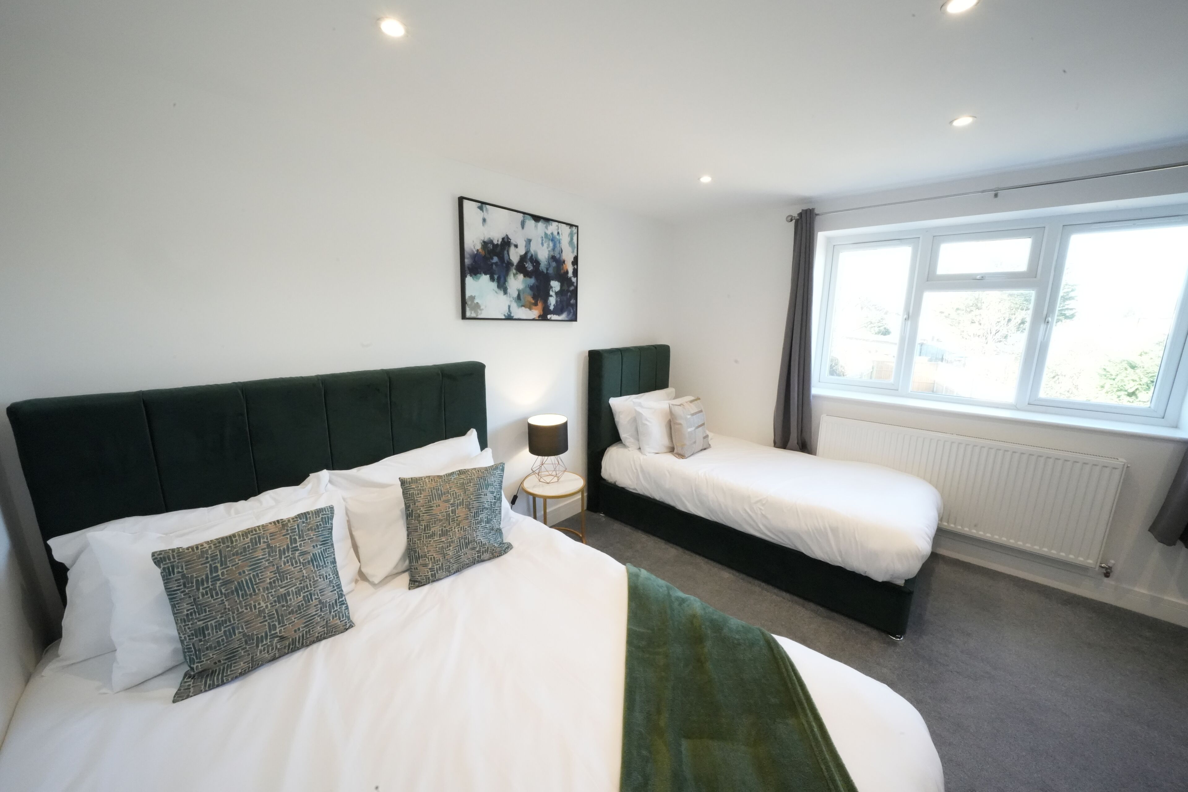 Quarto de hotel com duas camas, um quadro grande na parede e uma janela com cortinas.