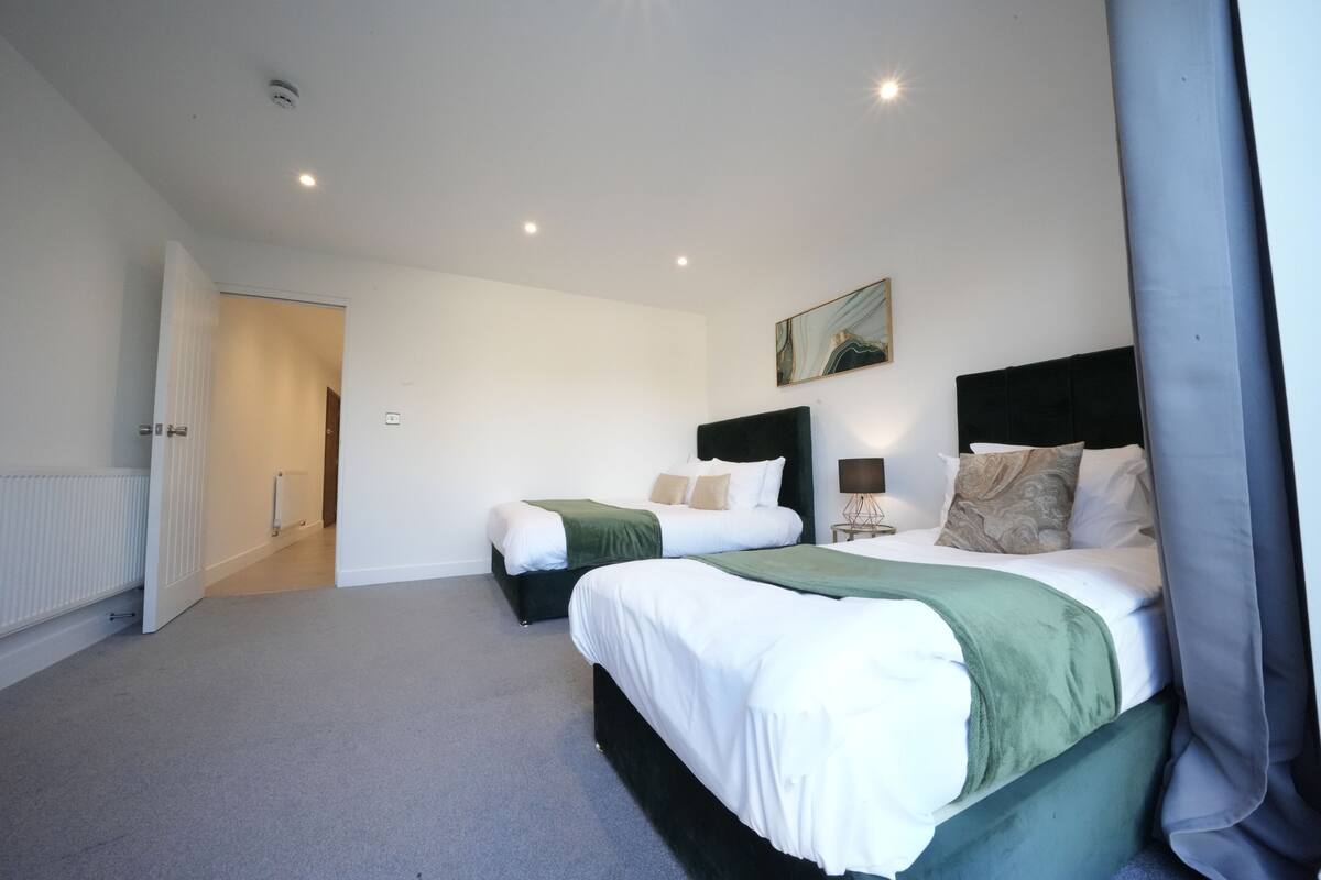 A modern hotel room with two beds, a large window, and a painting on the wall.