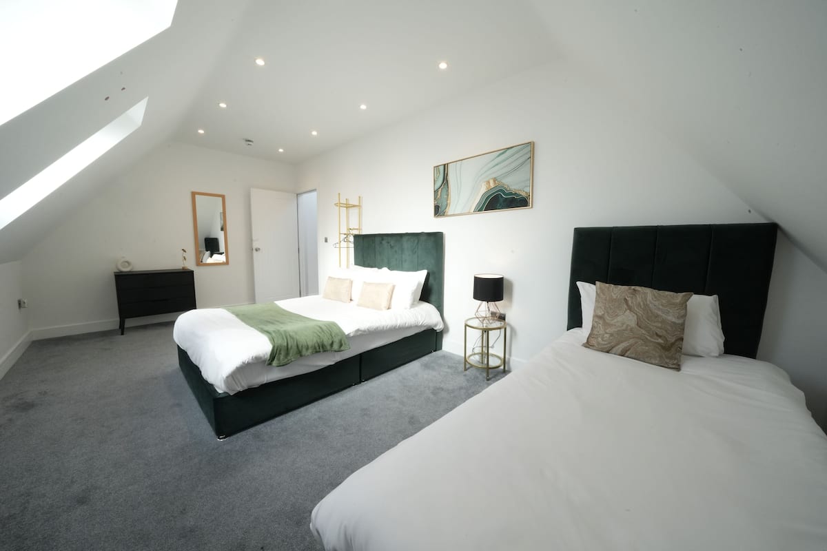 A bedroom with a skylight, a bed with a green headboard, a bedside table with a lamp, and a painting on the wall.
