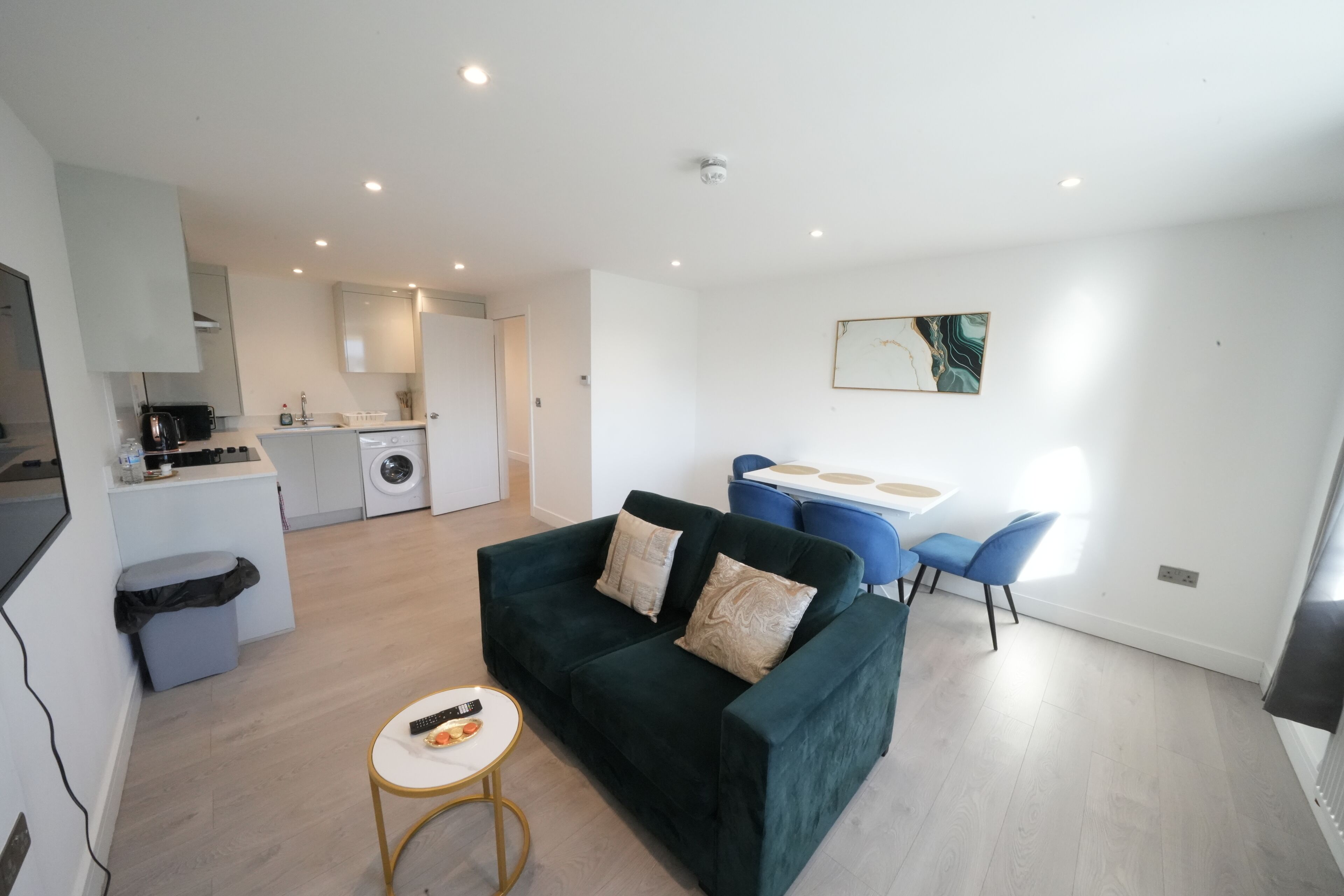 Een moderne woonkamer met een groene bank, een kleine ronde tafel, en een eethoek met blauwe stoelen.