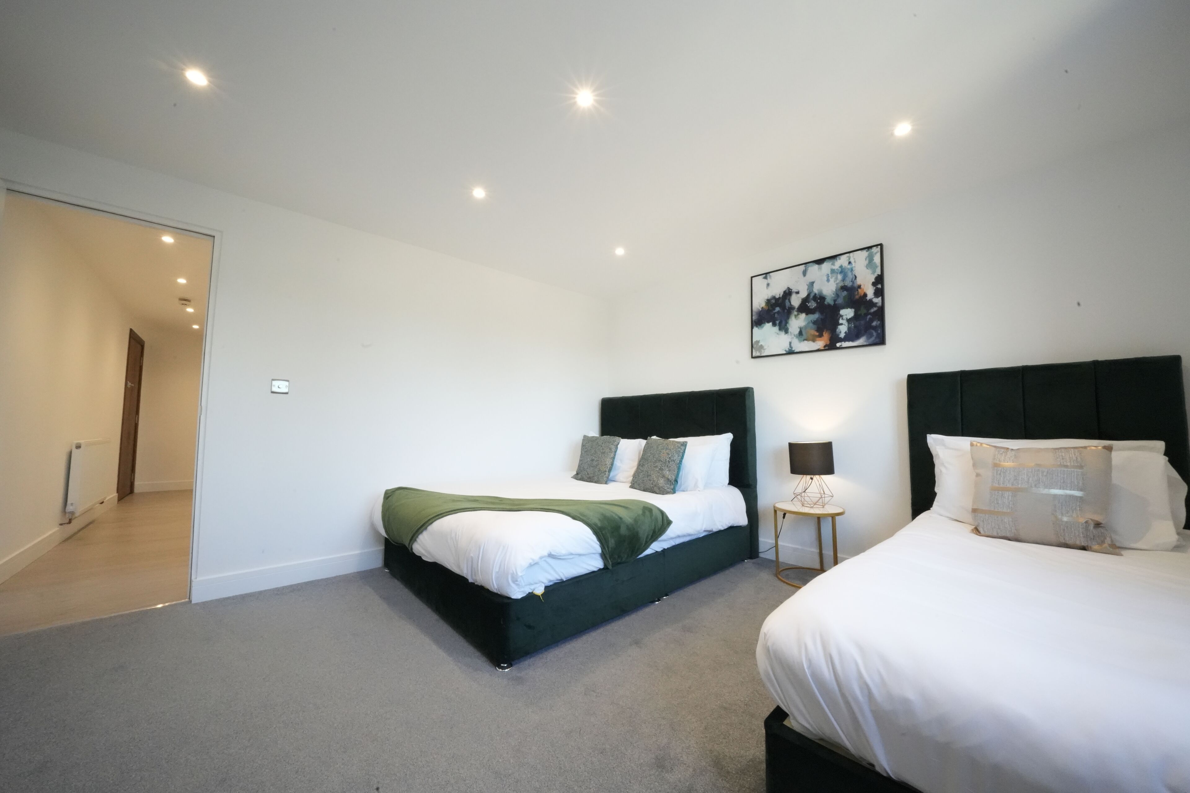 Ein modernes Schlafzimmer mit zwei Betten, einer grünen Decke auf einem Bett und einem Gemälde an der Wand.