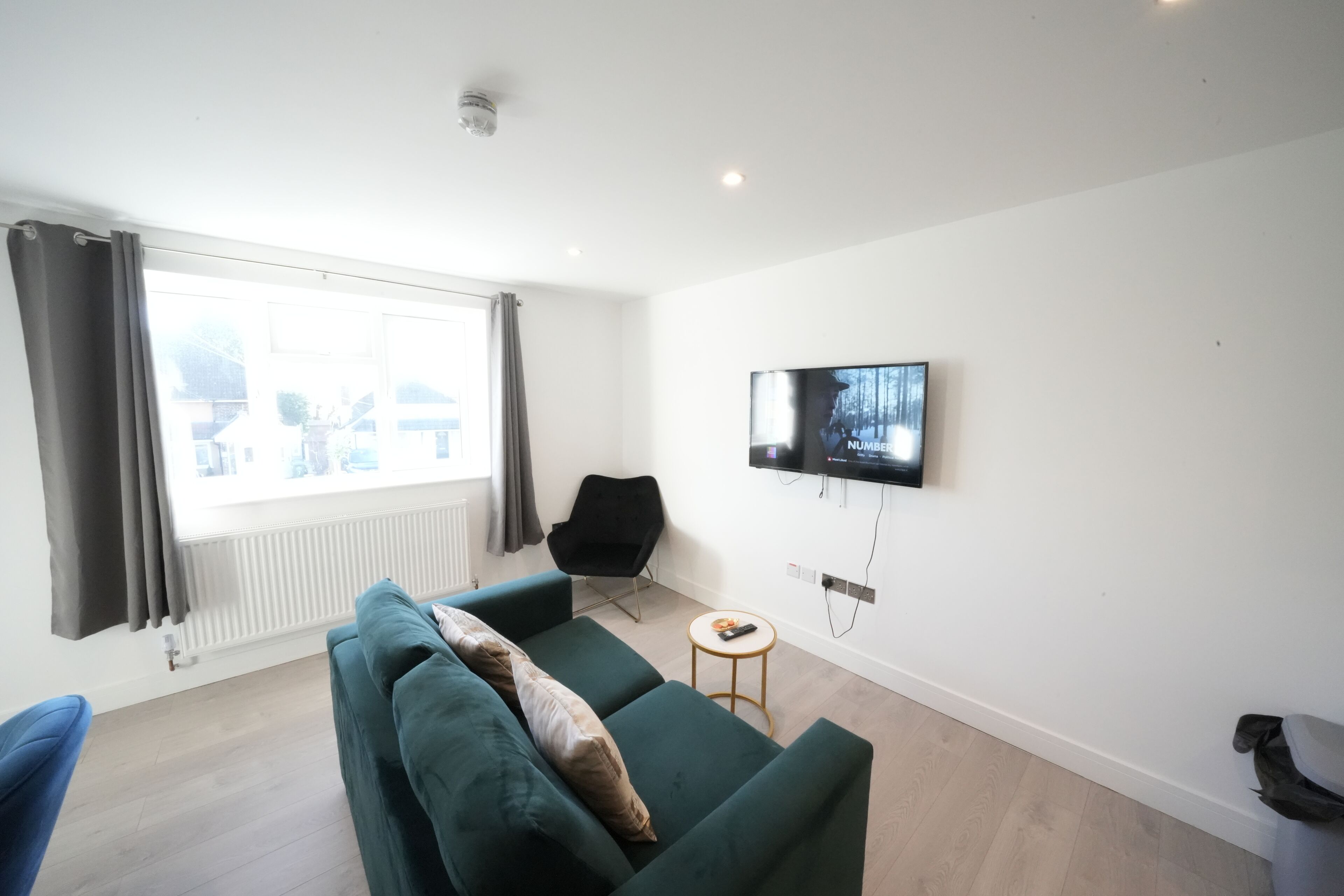 A modern living room with a green sofa, a black chair, a small round table, and a mounted TV.