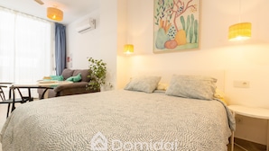 A bedroom with a large bed, a desk, and a chair. There is a plant and a painting on the wall. - Santa Pola Suites (Santa Pola)