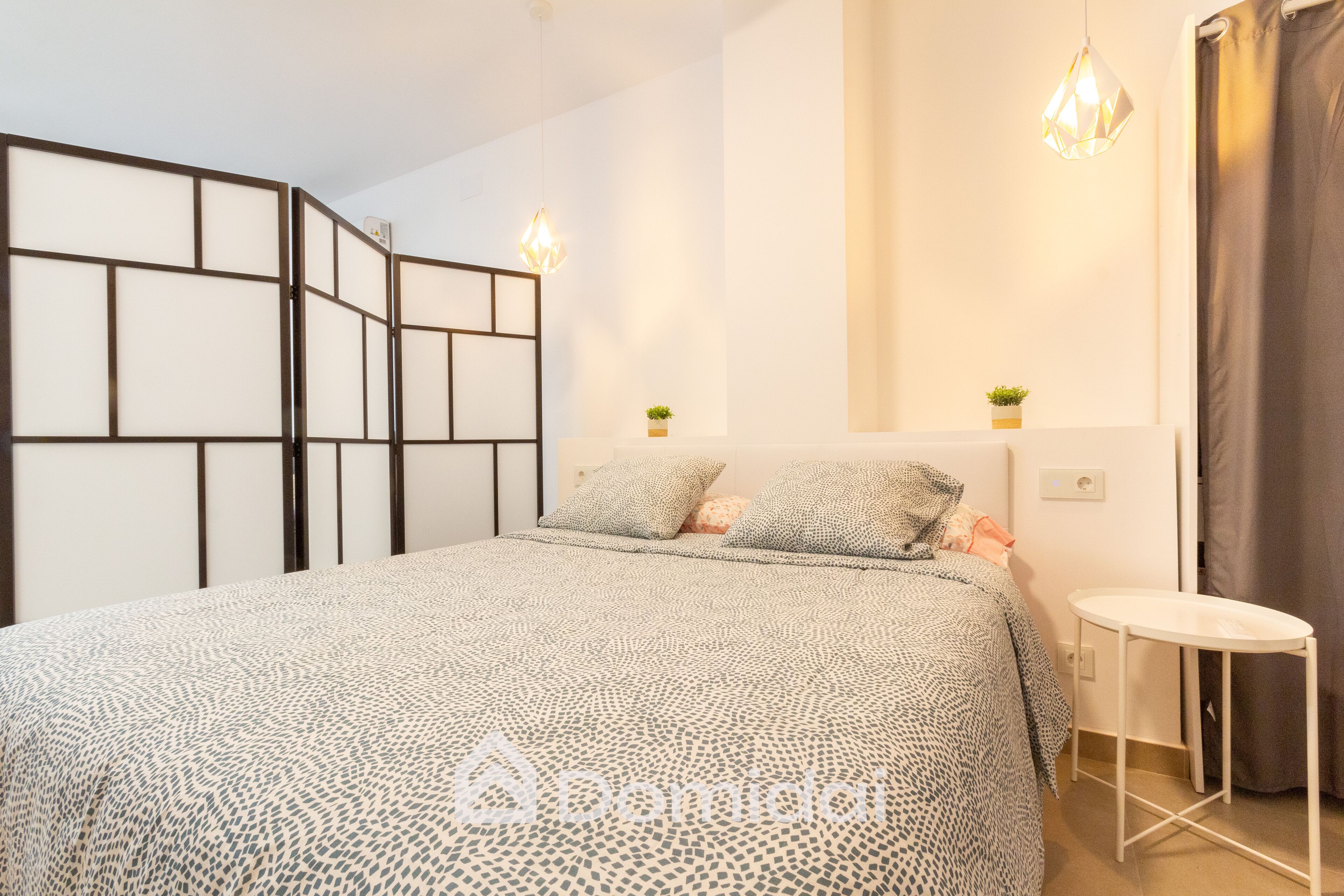 Un dormitorio con cama, mesitas de noche, una pequeña mesa y un separador decorativo.