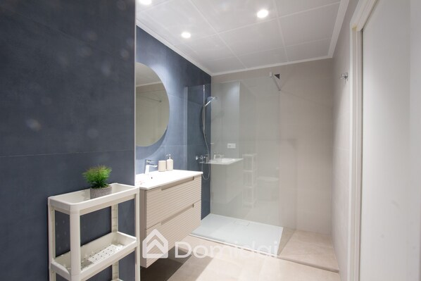 Un baño moderno con ducha de vidrio, tocador blanco con una planta y un espejo grande.