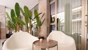 A modern hotel lobby with white chairs, a round table with pink candles, and large green plants. - Santa Pola Suites (Santa Pola)