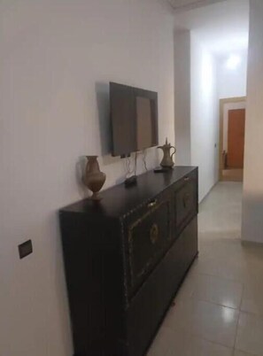 Simple, functional room with a dresser, flat-screen TV, and tiled floor.