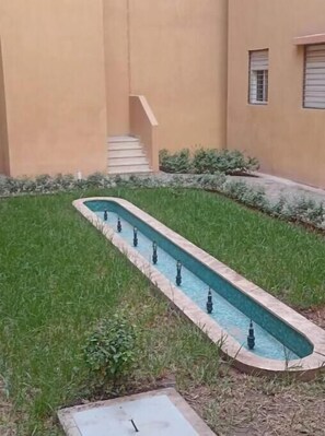 Stroll along the serene water feature, surrounded by lush greenery and a low stone wall.
