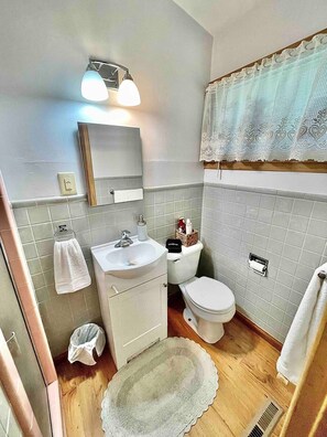 A bathroom with a sink, mirror, toilet, and a decorative lace window treatment. - Sunflower Retreat (Hutchinson)