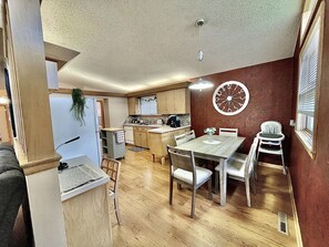 A compact kitchen with wooden cabinets, a dining table with chairs, and a clock on the wall. - Sunflower Retreat (Hutchinson)