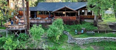 Una cabaña con terraza que da al río, rodeada de bosque y montañas.