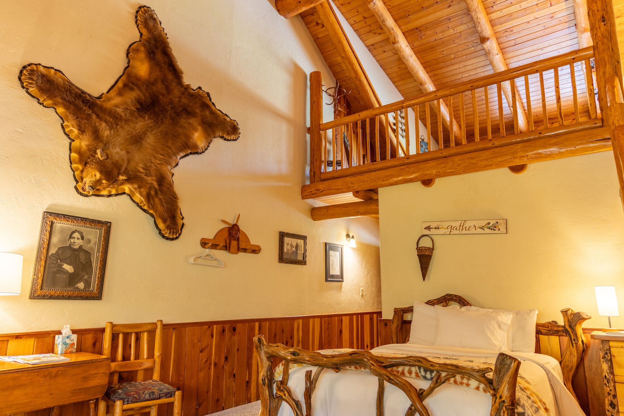 Ein rustikaler Raum mit einem Bett, Holzmöbeln, einem aufgehängten Tierfell und einem Balkon mit Holzgeländern.