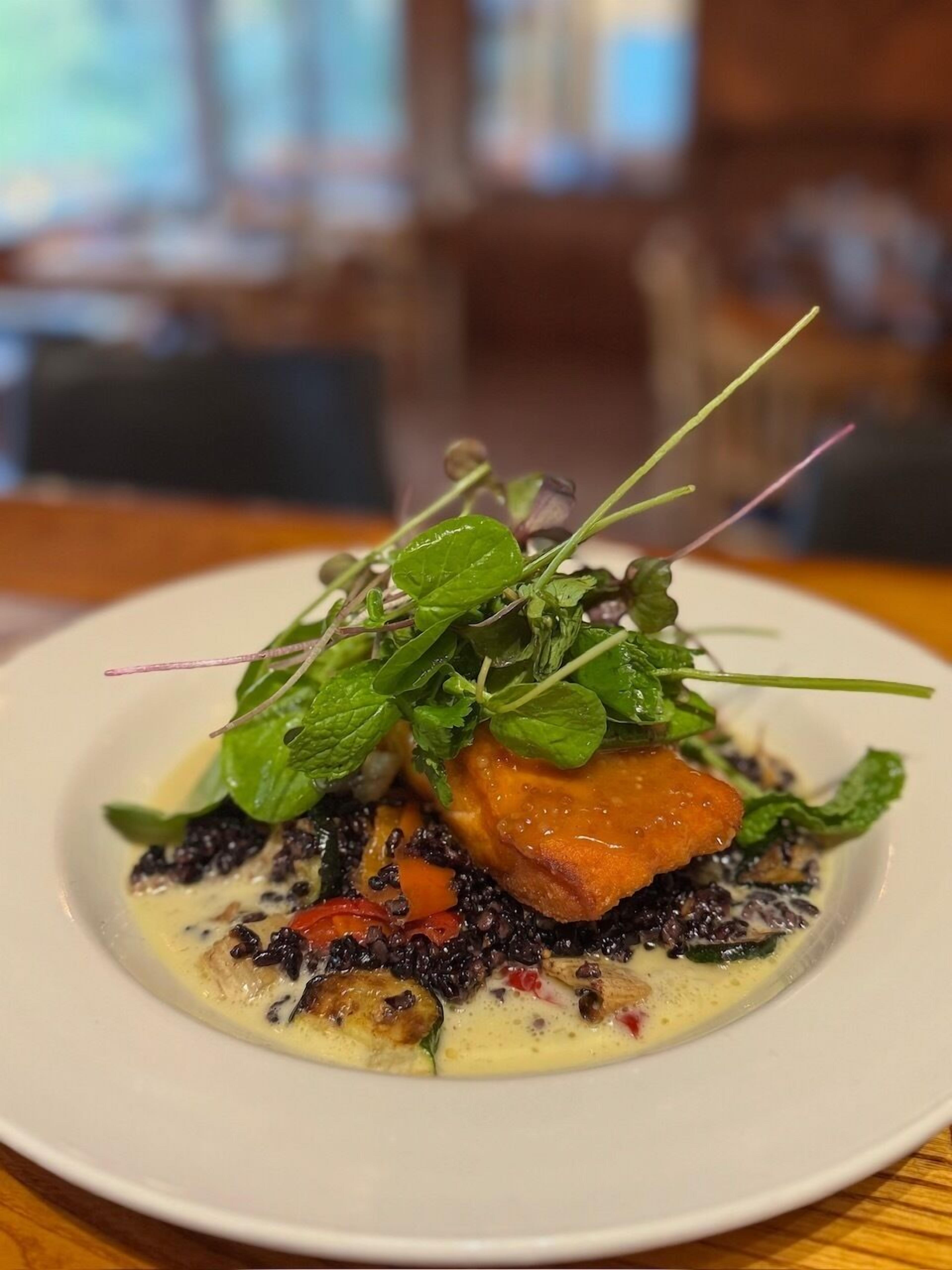 A plate of food with a variety of greens, a piece of salmon, and a creamy sauce.