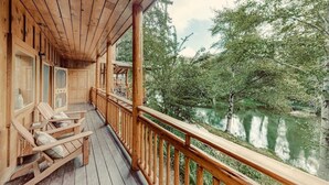 Une terrasse en bois avec une rambarde donnant sur une étendue d’eau calme, entourée d’arbres.