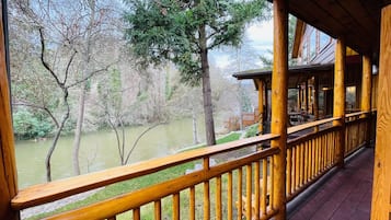 Une terrasse en bois dotée d’une balustrade, offrant une vue sur une rivière et une zone boisée.