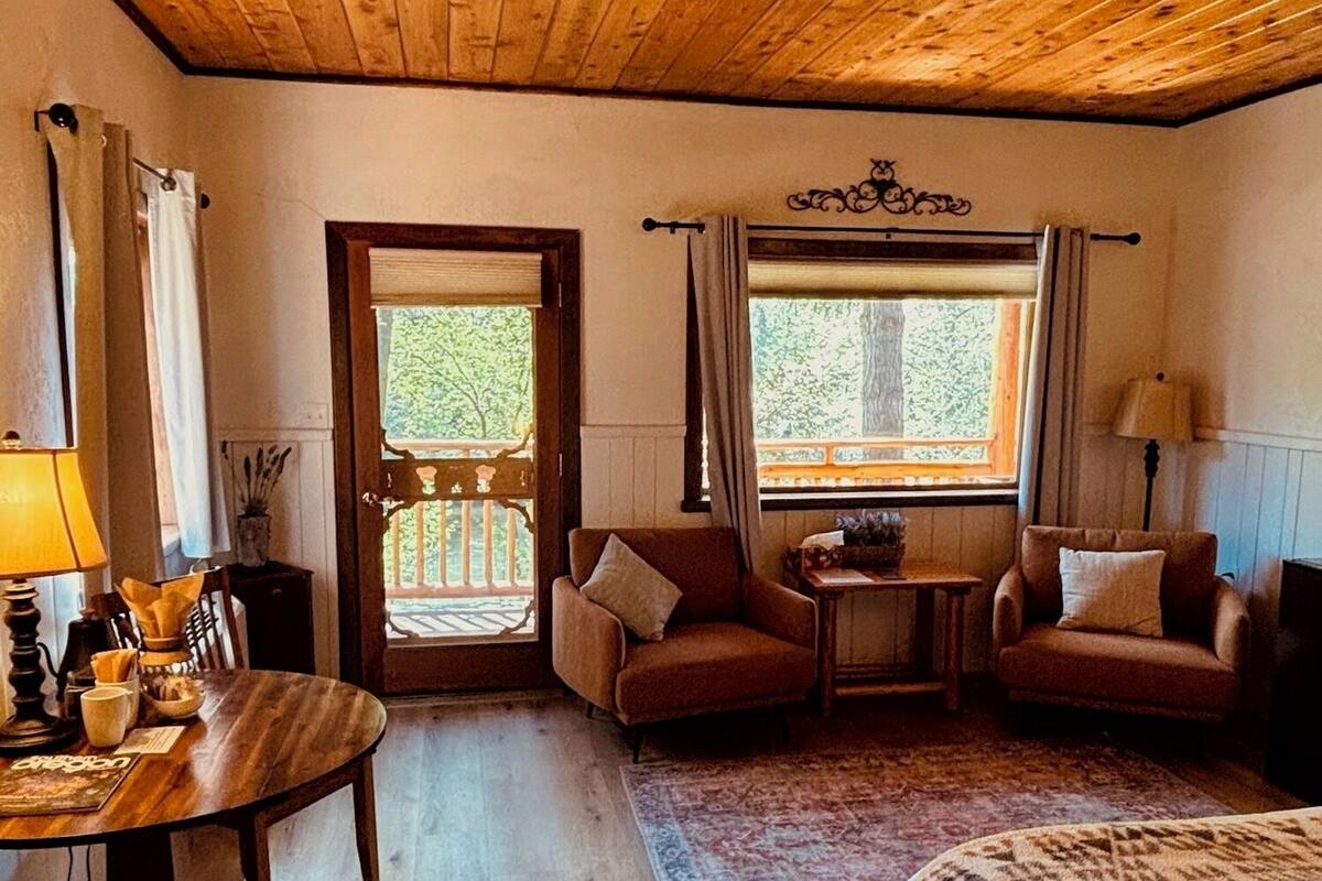 Een gezellige kamer met een houten plafond, een bed met een geborduurde deken, twee fauteuils, een tafeltje en een raam met gordijnen.