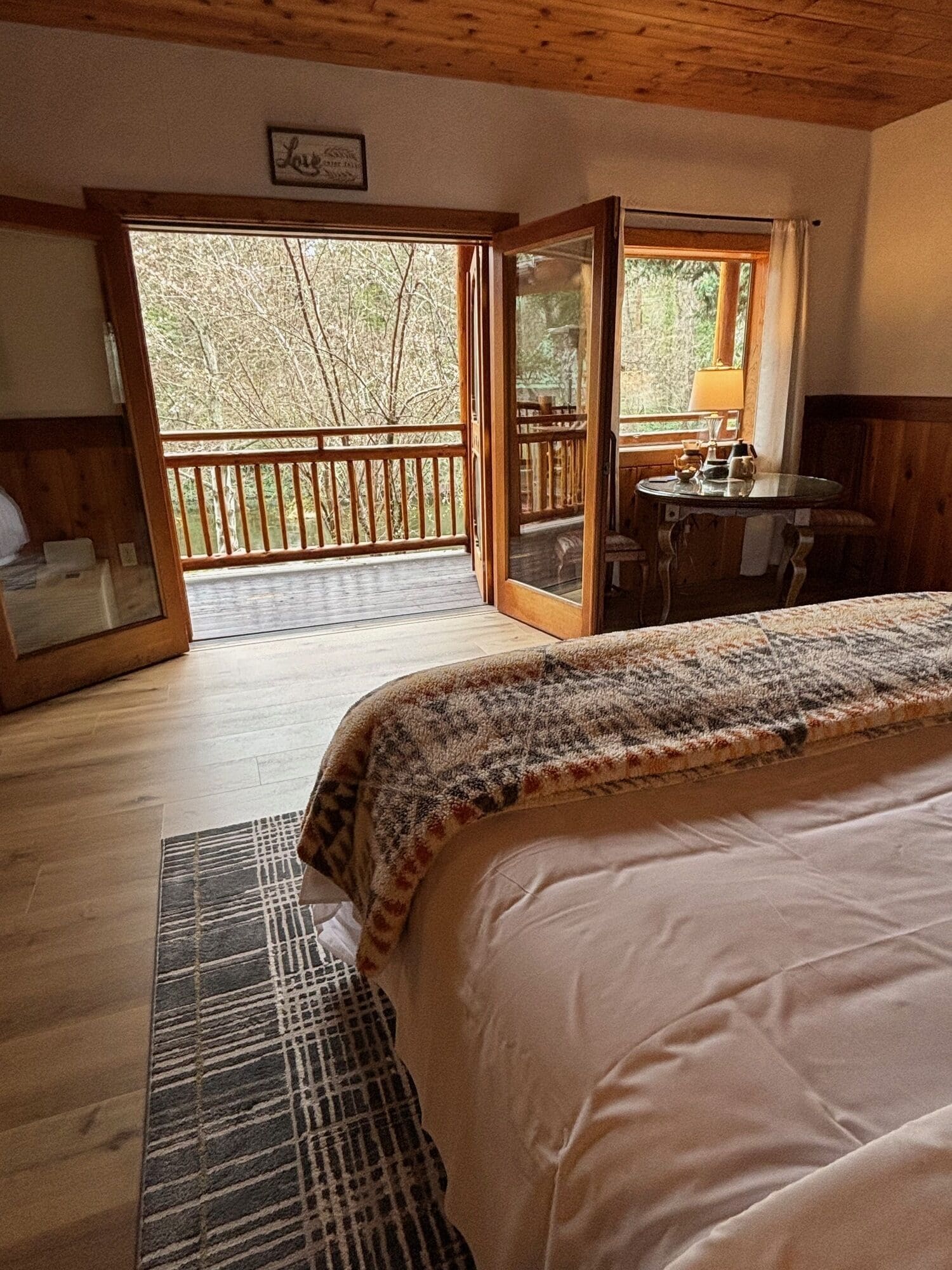 A cozy bedroom with a large bed, a wooden desk, and a view of the outdoors through a sliding door.