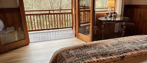 A cozy bedroom with a large bed, a wooden desk, and a view of the outdoors through a sliding door.