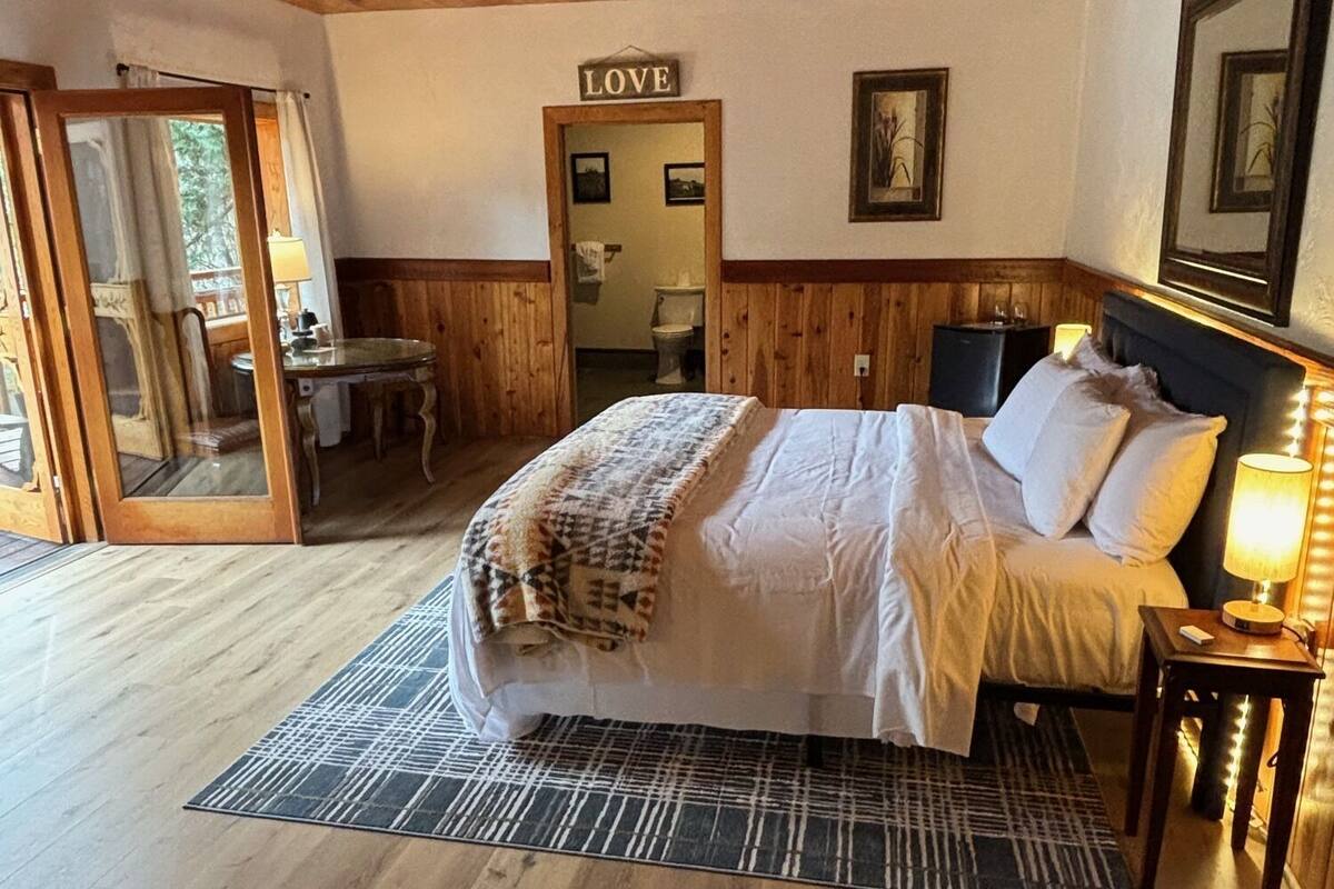 Een slaapkamer met houten lambrisering, een bed, nachtkastje, spiegel en een deur naar een badkamer.