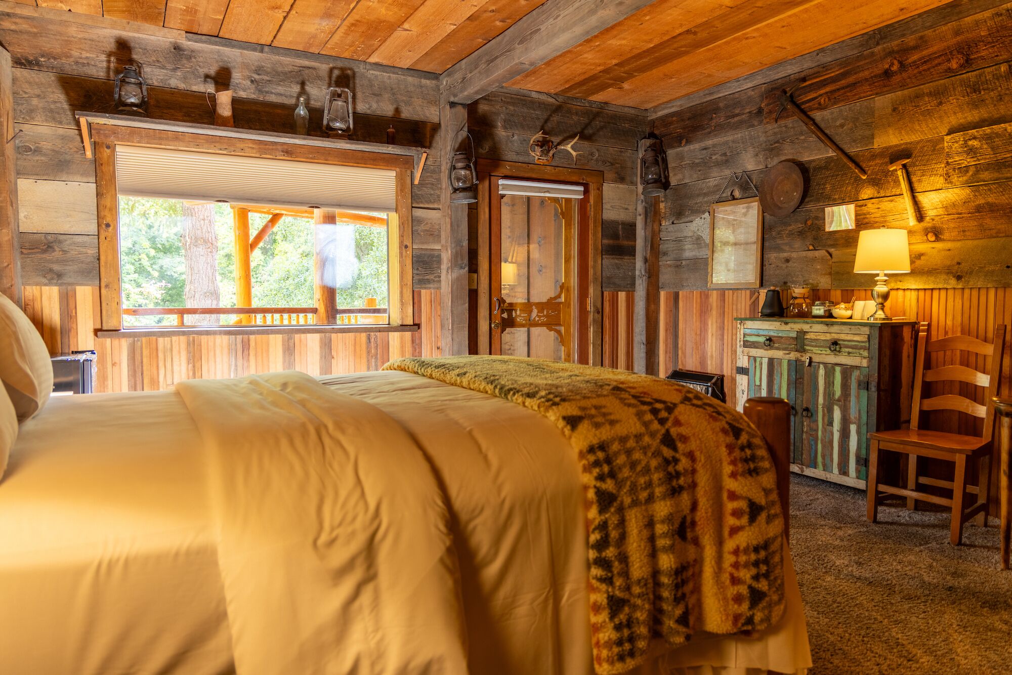 Una camera in legno dallo stile rustico, con un letto, una scrivania e una finestra che si affaccia sul verde.