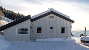 A snow-covered building with a sloped roof, large windows, and a chimney. - Idyllic cottage on a farm with fantastic views and surrounded by nature.  (Tretten)