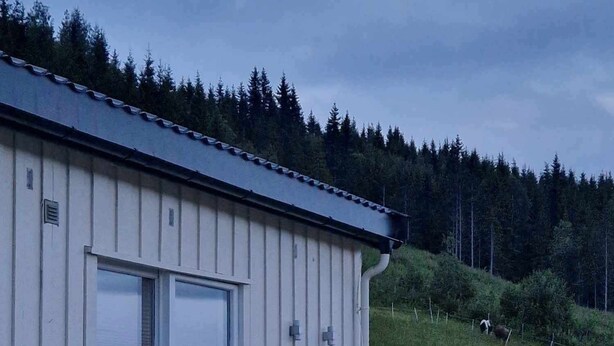 A white building with a large window and a wooden deck with lights. - Idyllic cottage on a farm with fantastic views and surrounded by nature.  (Tretten)
