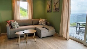 A living room with a sofa, two round tables, and a view of a deck and mountains. - Idyllic cottage on a farm with fantastic views and surrounded by nature.  (Tretten)