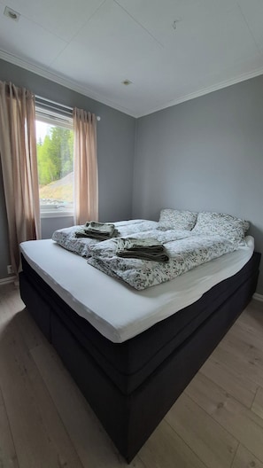 A bedroom with a large bed, a window with curtains, and a view of trees.