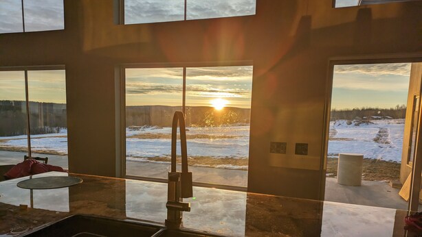 Een keuken met een groot raam met uitzicht op een besneeerd landschap in de zonsondergang.