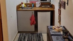 A compact kitchen with a microwave, sink, and small refrigerator. A window with lace curtains is above the sink, and a shelf with decorative items is on the wall. - Cute Studio near Yad Vashem. Free street parking. (Jerusalem)