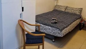 A bedroom with a bed, a chair, a wardrobe, and a wall with framed pictures. - Cute Studio near Yad Vashem. Free street parking. (Jerusalem)