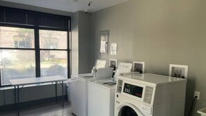 A laundry room with a large window, two washing machines, and a drying rack. - Studio63 on Phillips (Sioux Falls)