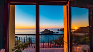 Un balcón con vista al mar al atardecer, destacando un promontorio rocoso y una montaña distante.