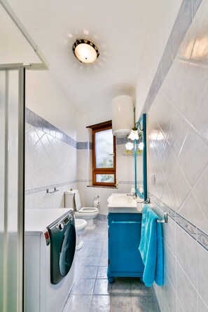 Une petite salle de bain équipée d’un lave-linge, de toilettes et d’un lavabo.