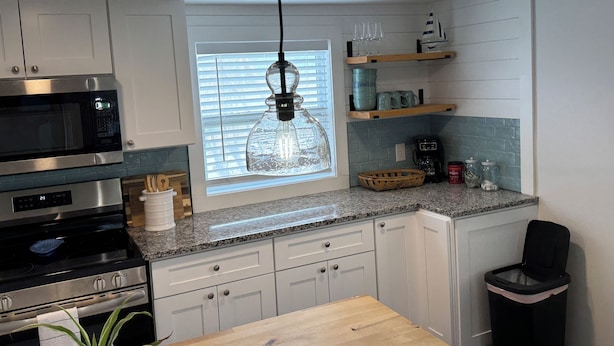 A modern kitchen with white cabinets, a stainless steel microwave, a built-in oven, a wooden dining table, and a hanging pendant light. - 1 Mile to Anna Maria Island, 2 bd rm 2 bath 3 Queen beds, sleeps 6 comfortably. (Bradenton)