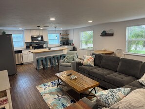 A modern kitchen with a central island, bar stools, a grey sofa, and a wooden coffee table.