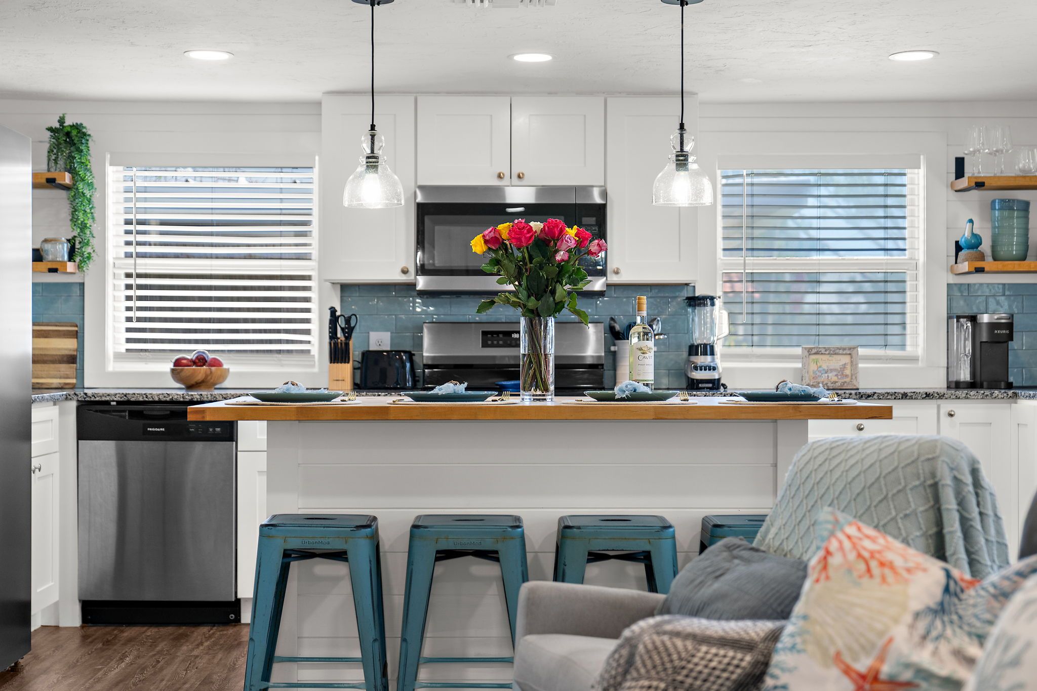 A modern kitchen with a central island, bar stools, and a dining area with a sofa.