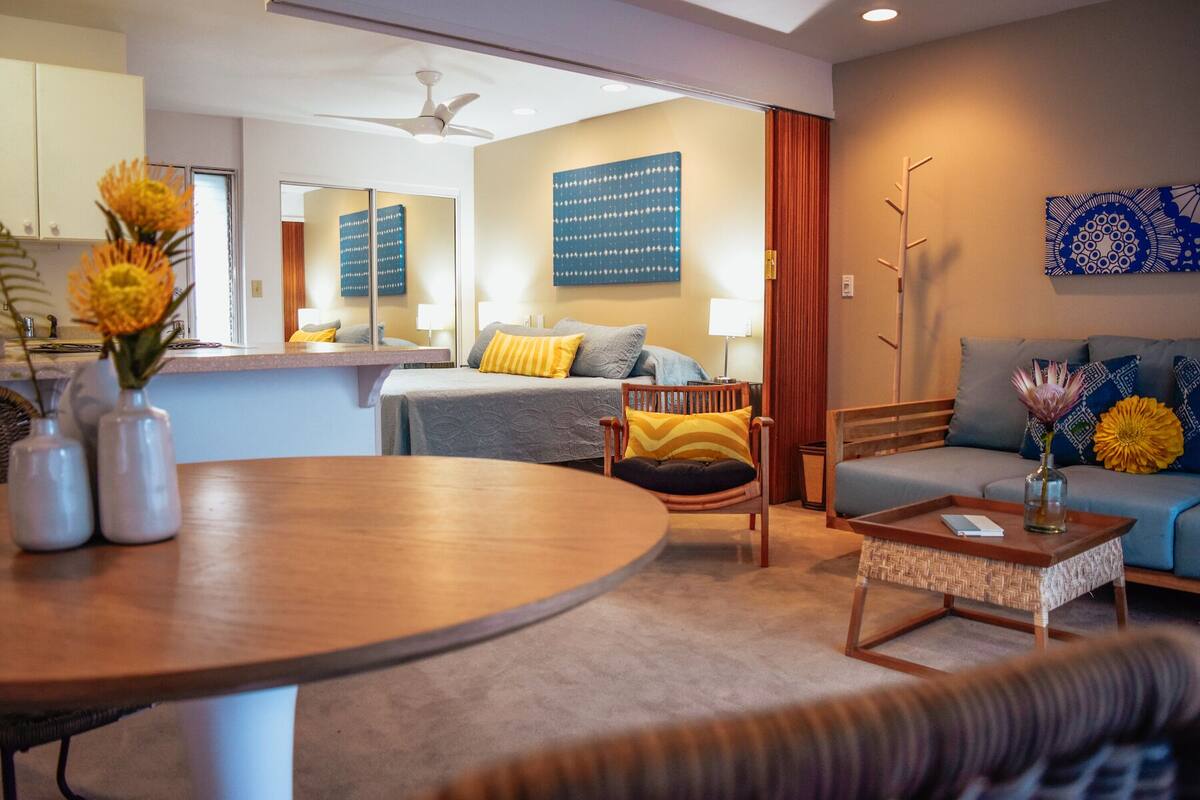 Een moderne hotelkamer met een ronde eettafel, een bank, een stoel en een bed met een blauwe hoofdgreep.