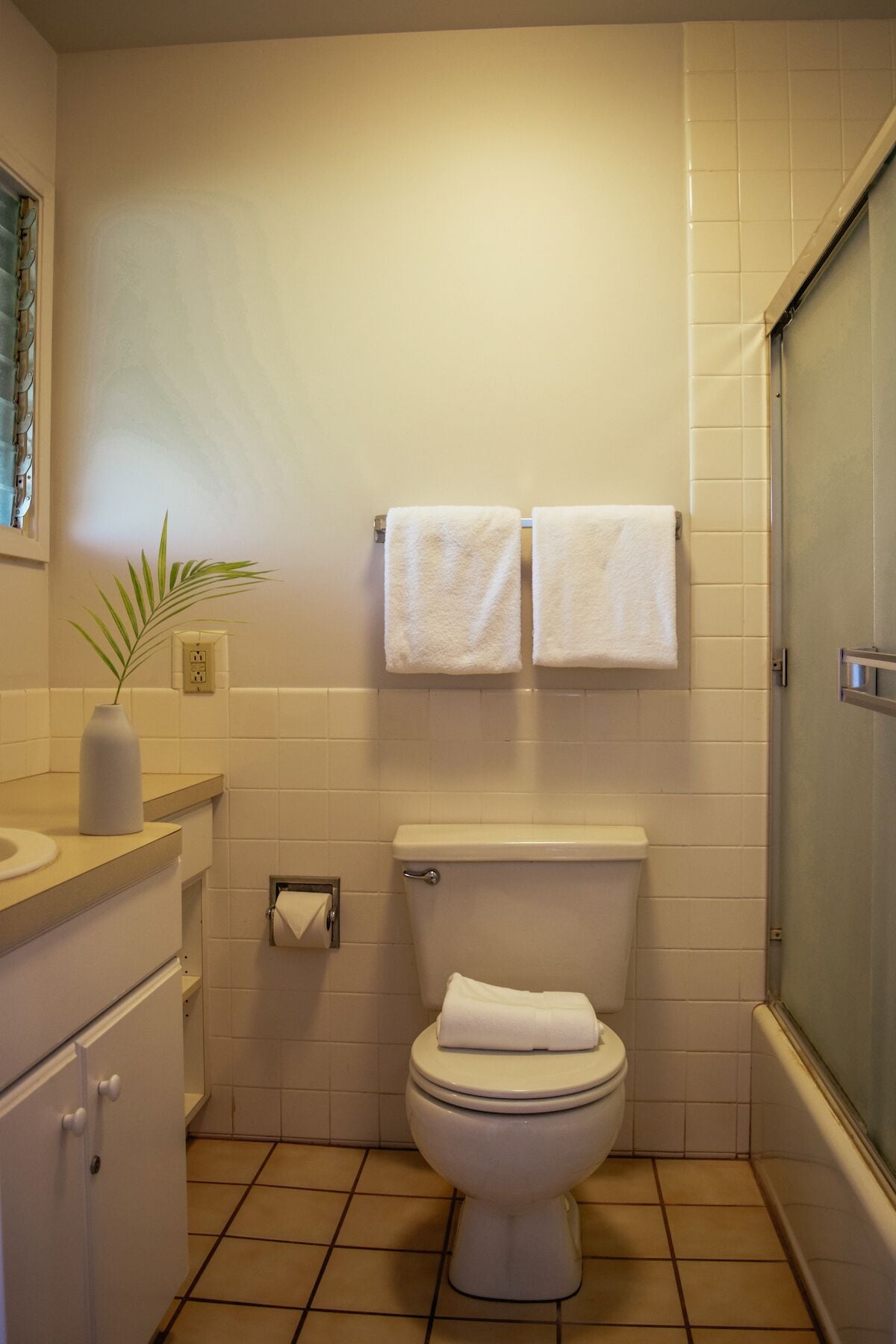 A bathroom with a toilet, two towels hanging on the wall, a sink with a vase, and a shower area.