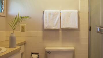 A bathroom with a toilet, two towels hanging on the wall, a sink with a vase, and a shower area.