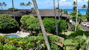 Un edificio con piscina, rodeado de vegetación tropical y palmeras, con vistas a un océano azul y despejado.