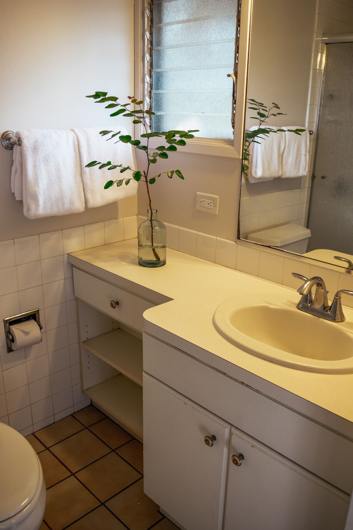 A bathroom with a white sink, a mirror, a toilet, and a plant in a glass vase.