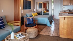 Habitación moderna y luminosa con cama, sofá, sillón, una mesita y una zona de cocina.