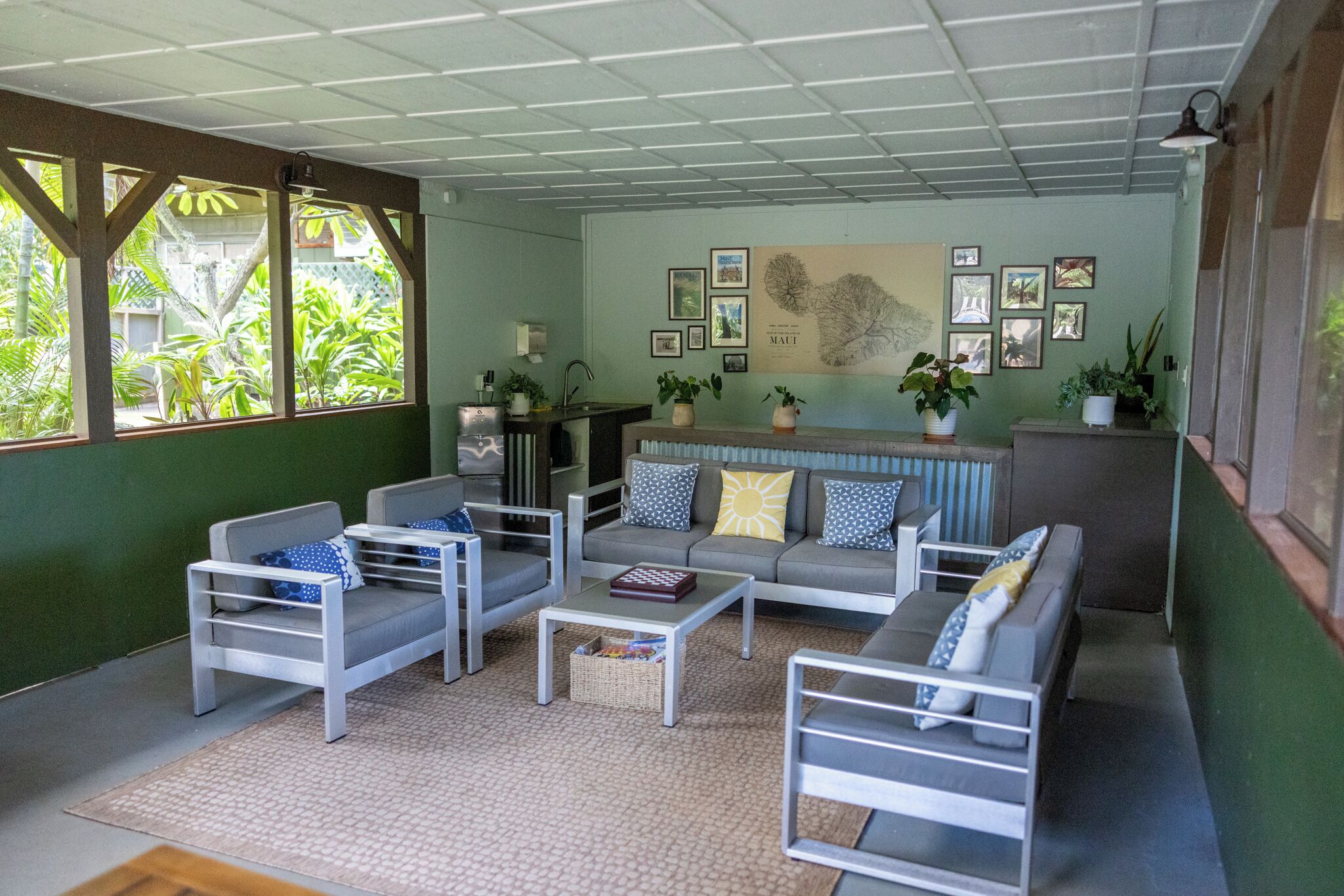 Un salon moderne avec un canapé, des fauteuils et une table basse. Des plantes en pot et des tableaux encadrés décorent les murs.