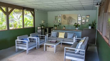 Un salon moderne avec un canapé, des fauteuils et une table basse. Des plantes en pot et des tableaux encadrés décorent les murs.